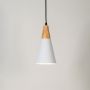 White cone pendant light with wooden top glowing on white background.