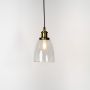 Clear glass pendant light with brass and black holder turned on glowing softly on plain white background.