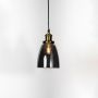 Smoked glass pendant light with brass and black holder turned on glowing softly on plain white background.
