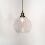 Clear glass globe pendant light with brass and black holder turned on glowing softly on white background.
