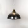 Smokey glass dome pendant light glowing on white background with brass and black fitting for interior lighting.