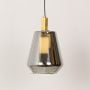 A tapered smoked glass pendant hanging on a white backdrop with the light on creating a soft warm glow through the transparent reflective glass surface.