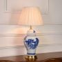 Blue and white ceramic table lamp illuminated on white background with pleated fabric shade and brass base for timeless home lighting.