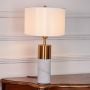 White marble and brass table lamp illuminated on white background with fabric shade offering warm modern bedside or console lighting.