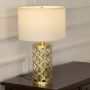 White shade gold lattice table lamp on wooden sideboard with light on and white panel wall background for chic contemporary home décor.