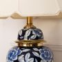 Close view of floral ceramic lamp showcasing detailed craftsmanship with gold base and elegant cream fabric shade for timeless appeal.