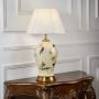 Ivory ceramic lamp with bird and flower motifs and golden base displayed with light on against plain white background.