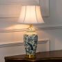 Ivory ceramic lamp with blue floral bird artwork and pleated white shade displayed lit on plain white background.