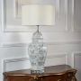 Ceramic table lamp with floral patterned base and white drum shade lit on white wall background table lamp.