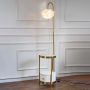 Modern gold floor lamp with feather shade and round glass table turned on glowing against white background.