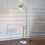 Contemporary gold floor lamp with round side table and marble base with light turned on on white background.