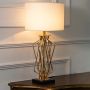 Gold twisted metal table lamp with illuminated white drum shade shown on a white background ideal for living rooms bedrooms and stylish console decor.