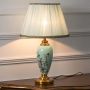 Elegant mint green floral ceramic table lamp turned on against white background with soft warm light diffused through pleated shade.