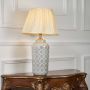 Ceramic table lamp with geometric grey pattern and cream pleated shade glowing softly against a clean white background.