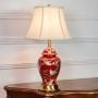 Red ceramic table lamp featuring detailed bird floral artwork gold metal base and white fabric shade displayed on white background.