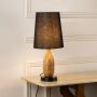 Amber glass table lamp with black fabric shade glowing softly on white background adding warm elegant lighting to living room decor.