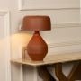 Brown ceramic table lamp with sculptural base and fabric shade placed on console creating soft ambient lighting for interiors.
