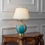 Turquoise ceramic table lamp with gold detailing and pleated white lampshade illuminated on white background for modern home lighting.