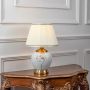 Ceramic table lamp turned on with pleated fabric shade and golden base displayed on clean white background.