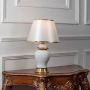 White ceramic table lamp turned on with tapered fabric shade and brass detailing displayed on white background.