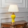 Yellow ceramic table lamp turned on with pleated fabric shade and brass detailing displayed on white background.