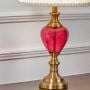 Closeup of red glass table lamp with heart shaped body brass detailing and pleated fabric lampshade.