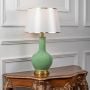 Green ceramic table lamp turned on with fabric shade and brass detailing displayed on clean white background.