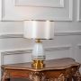 White ceramic table lamp turned on with fabric drum shade and brass detailing displayed on clean white background.