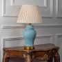 Blue ceramic table lamp with golden base and cream pleated shade on white background.