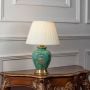 Green ceramic table lamp turned on with pleated fabric shade and floral hand-painted base displayed on white background.