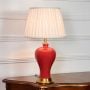 Red ceramic table lamp featuring smooth glossy finish gold metal base and pleated fabric shade displayed on white background.