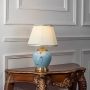 Lotus table lamp turned on with blue ceramic floral base and pleated shade on white background.