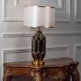 Black and gold striped table lamp with white shade turned on against plain white background.