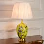 Yellow ceramic table lamp featuring floral bird design gold metal base and pleated fabric shade displayed on white background.