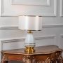 White shade gold base lamp on carved console table with light on and white wall panels for elegant bright décor.