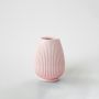 Soft pink ribbed ceramic vase with dried pine and grass stems against a clean white background for minimalist decor.