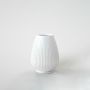 White ribbed ceramic vase placed on a white background highlighting its smooth glossy texture and elegant curved design.