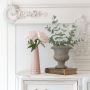 Pink ceramic vase with gold detailing placed on a white shelf against a patterned wall adding a soft modern touch to living room decor.