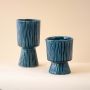 Set of blue textured pedestal vases arranged together creating a coordinated modern decor look with matching vertical lines and sculptural shapes.
