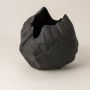 Closeup of black ceramic vase showing matte stone-like texture and organic handcrafted curves for modern artistic appeal.