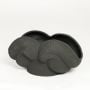 Black ceramic sculpted decorative bowl with layered curved texture isolated on white background for contemporary home decor use.