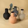 Modern ceramic pitcher collection in cream black gray and peach with metal handles holding eucalyptus stems on warm neutral display.