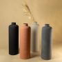 A set of tall cylindrical floor vases in terracotta black beige and grey arranged together with pampas grass creating a coordinated earthy decor collection.
