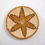 Round woven basket wall decor on white background with starburst design in beige and brown handmade natural materials.