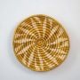 Round wicker basket wall decor on a clean white background showing natural handwoven craftsmanship with beige and brown tones highlighting artisan detail.