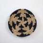Handwoven wicker wall decor plate in beige and black round natural fiber spiral design light on white background for styling.
