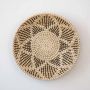 Handwoven wicker basket wall decor with black and beige star pattern design on white background for home decoration.