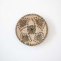 Handwoven wall basket decor in natural and black tones with boho design on white background.