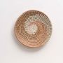 Handwoven wall basket in natural and pink fiber with rustic boho design shown on white background.