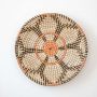Handwoven wall basket in natural orange and black fiber with geometric design shown on white background.